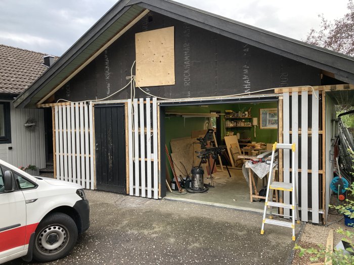 Renovering av husets fasad med ny panel delvis uppsatt och byggnadsställning framför garage.