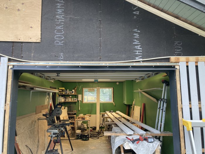 Garage under renovering med verktyg och träplankor, isolermaterial på väggen och en stege.
