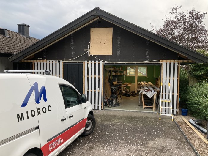 Garage under renovering med oskyddade väggsektioner, ny uppsatt träpanel och renoveringsmaterial synligt.