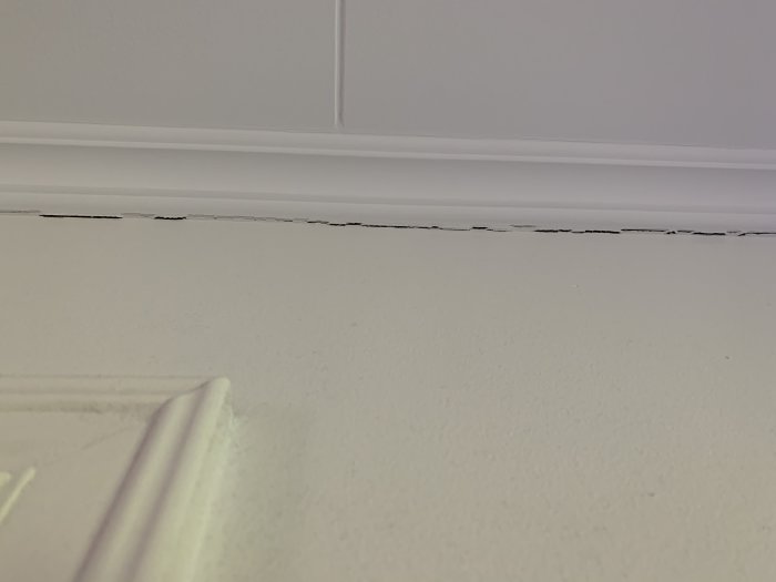 Taggig spricka i skarven mellan vitmålad taklist och vägg i ett hus från 2015.