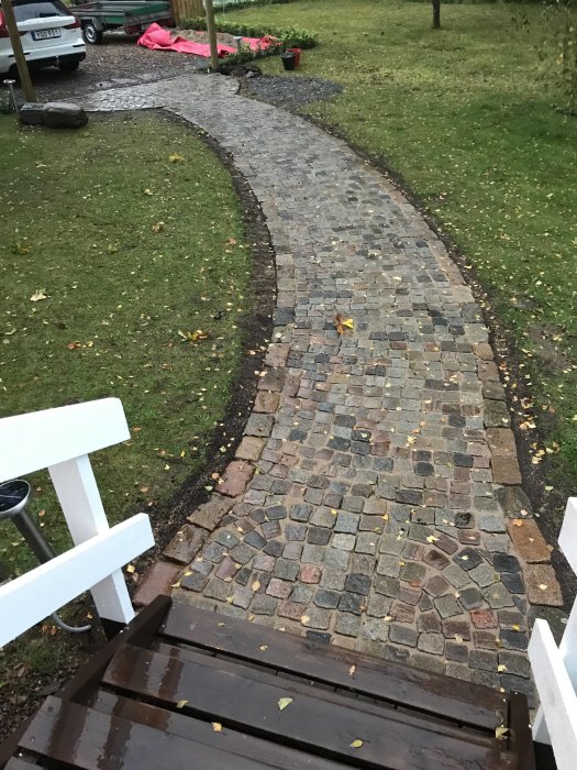 En nylagd stenlagd stig i en trädgård som slingrar sig från en trätrappa, omgiven av grönt gräs och löv.