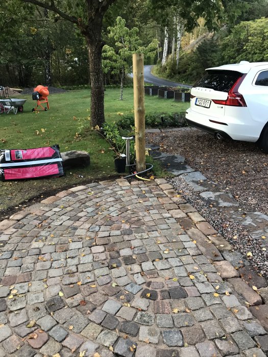 Nyklagd stenläggning vid entrégång med oregelbundna stenar, en parkerad bil och trädgård i bakgrunden.