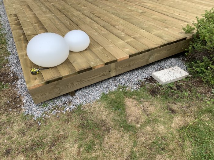 En nästan färdigställd träaltan med en måttband på och stenlagd grund runt omkring, intill en vit stentrappa.