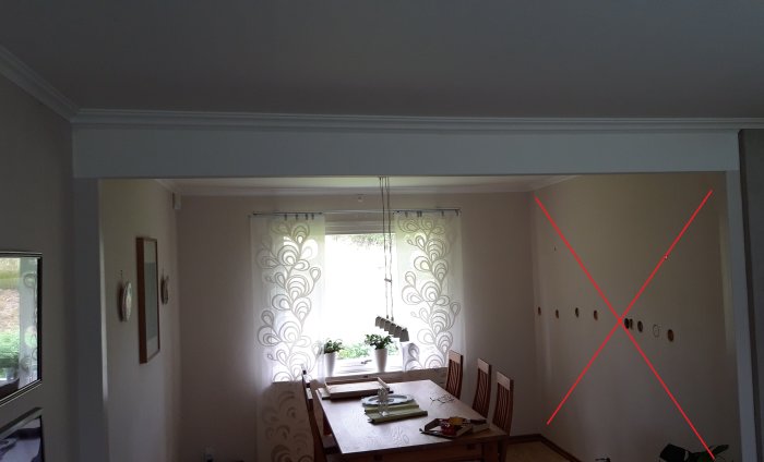 Ruokailuhuone, jossa on ikkuna ja verhot. Punainen X seinällä osoittaa mahdollisesti purettavaa seinää. Pöydällä on koriste-esineitä.