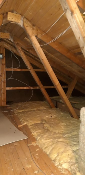 Puinen ullakkorakenne, jossa näkyy kattotuolit ja eristys. Kattorakenne liittyy keskusteluun mahdollisesta kantavan seinän poistamisesta.