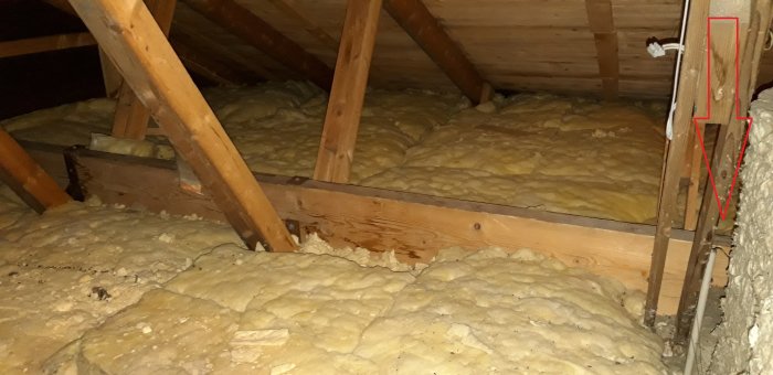 Puutarvikkeet ja eristys ullakolla. Pystypalkit tukevat kattoa, osittain näkyvä laminoitu puupalkki.