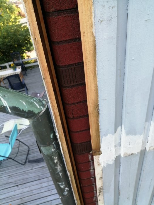 Renovering avslöjar röd beklädnad med tegelmönster under träpanel på husvägg.