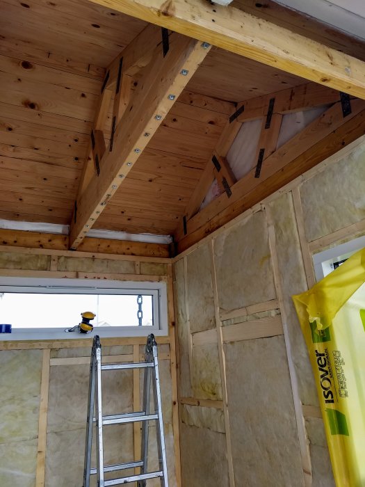 Inredning av en veranda under konstruktion med synlig isolering, träpaneltak och en stege mot väggen.