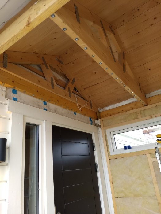 Kall veranda under isolering med trä paneltak, vindskydd och ventil, samt ytterdörr.