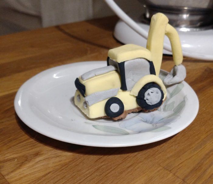 Tårtdekoration föreställande en grävmaskin gjord av sockerpasta på en vit tallrik.
