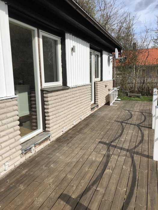 En vitputsad villa med svart tak och träveranda under soligt vårväder.