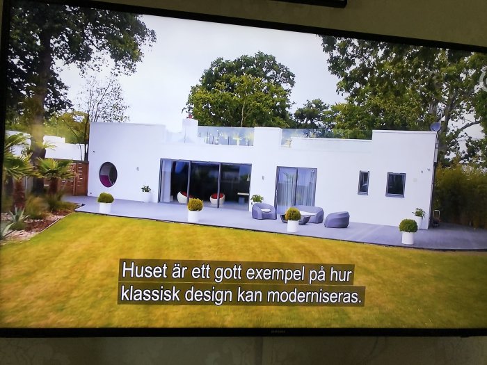 Vit modern villa med stora fönster och minimalistisk trädgård, projicerad på en TV-skärm.