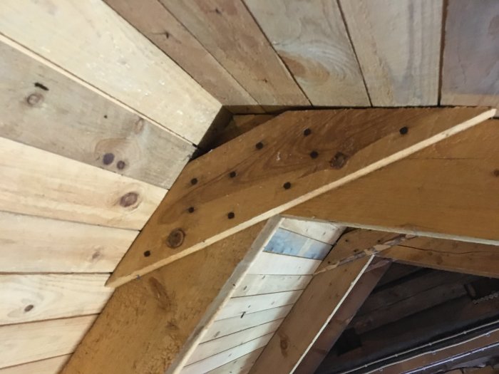Träkonstruktion av takstol inne i timmerstuga visande horisontella reglar och takbjälkar.
