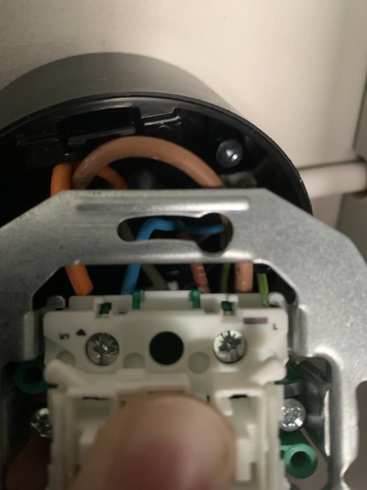 Närbild av en hand som håller en transformator med synliga elektriska anslutningar och kablar i en installationsdosa.