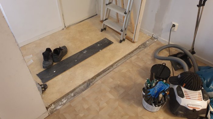 Golv med ett tomrum efter en rivet vägg mellan plastgolv, arbetsmaterial och verktyg syns.