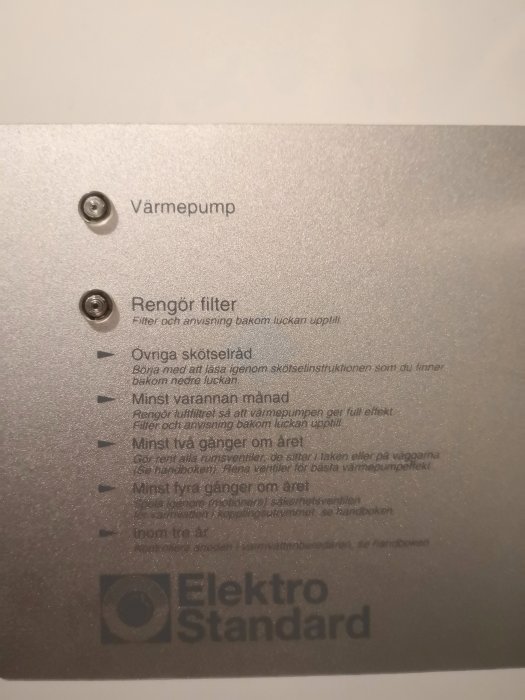 Instruktionskylt på en värmepump med underhållsanvisningar och företagslogotyp.