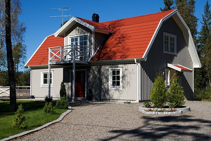 Ett grått hus med rött tak, balkong med fyra stolpar och en främre trädgård.