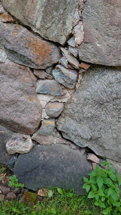 Skadad grundmur med lösa stenar och synliga håligheter, behov av reparation.