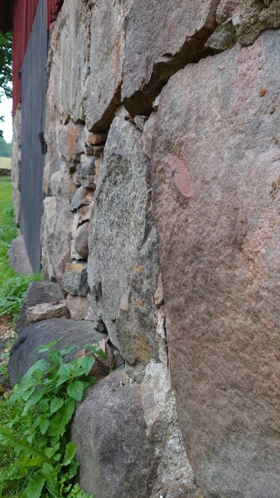 Slitna stora stenar i en gammal grundmur med synliga sprickor och utbrutet murbruk.