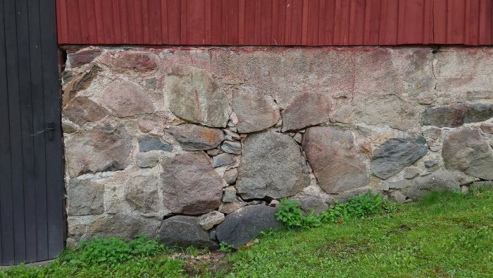 Stenmur vid en byggnad med synliga skador och utsläppt fog, behöver repareras.