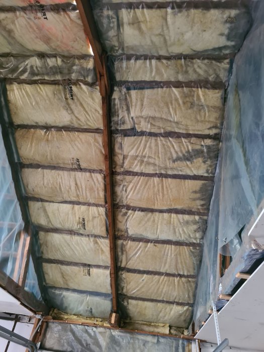 Oisolerad garagetak med träreglar och mineralull isolering täckt av plast, redo för renovering.