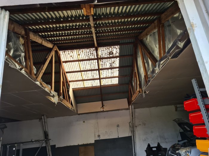 Inredning av ett garage med synliga träbjälkar och plåttak innan renovering.
