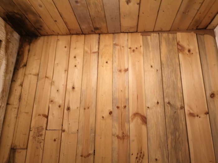 Obehandlade träplankor på ett golv före en badrumsrenovering.