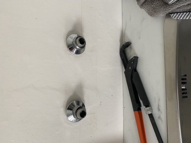 Två utstickande rör med invändiga tappar i en tvättstuga, bredvid en rörtång.
