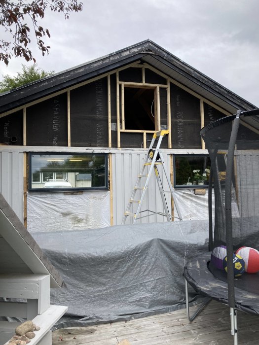 Renoverat hus med vindslucka flyttad till baksidan, stege placerad framför, och en studsmatta i förgrunden.