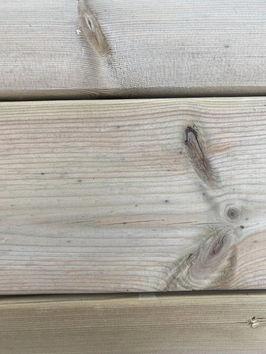 Nytillverkad altan i trä med synliga mörkgröna prickar nära fasaden.