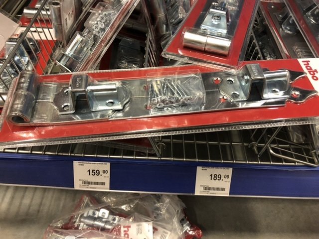 Förpackning med gångjärn och skruvar i en butikshylla, prismärkt 159 kronor.