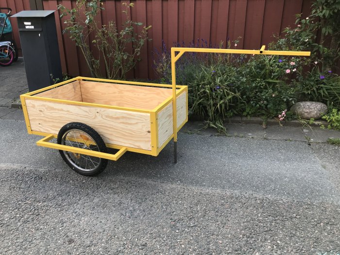 Nybyggd gul och träfärgad cykelkärra parkerad bredvid en trädgård.