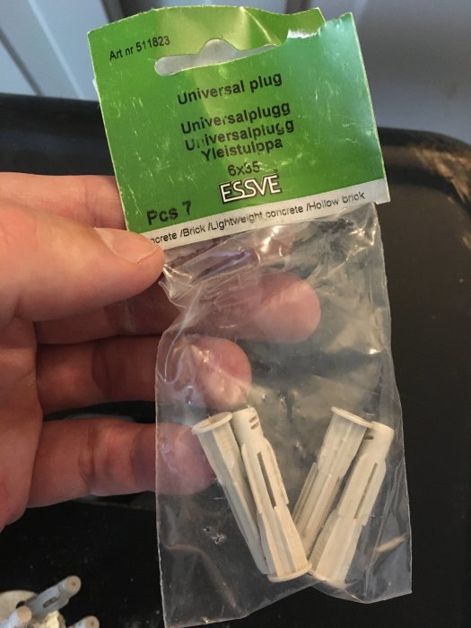 Hand håller en förpackning med oexpanderade universaldübel och synlig längdskillnad till skruven.