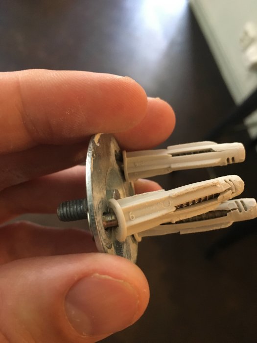 Närbild av en hand som håller en väggfäste med tre oexpanderade pluggar och en skruv, visar längdskillnaden.