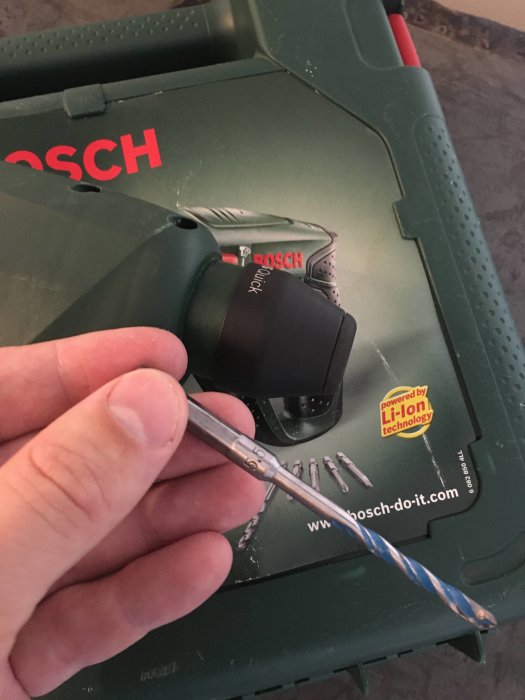 Hand håller en 5,5 mm borr framför en Bosch borrmaskinsväska.