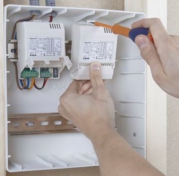 Händer installerar ett drivdon i en vit infälld elektrisk låda på en vägg.