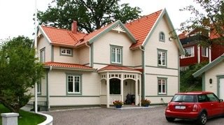 Nybyggd vit villa med rött tak från Karlsonhus, parkerad röd bil framför, i ett bostadsområde.