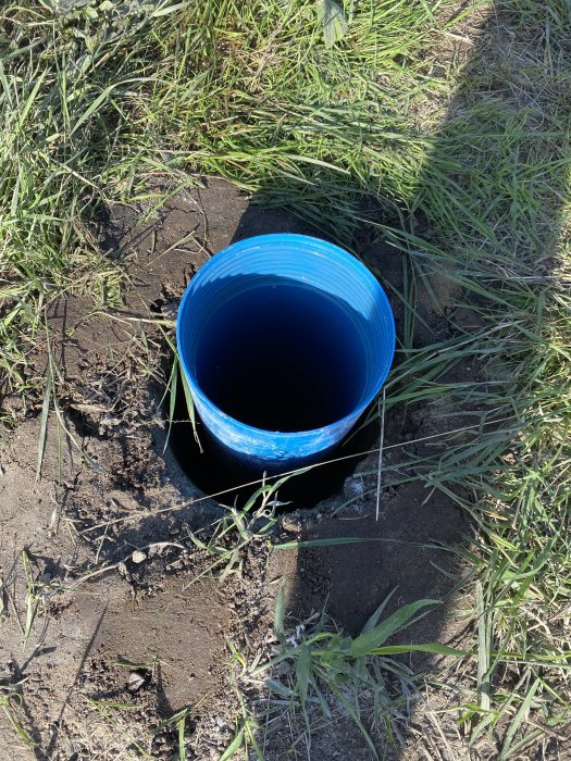 Blå plastbrunn utan synligt innehåll installerad i marken omgiven av gräs och jord.