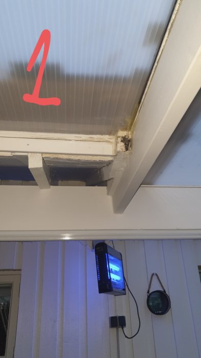 Vattenläckage vid anslutningen mellan takplåtar och vitmålad vägg, markerad med röd siffra 1.