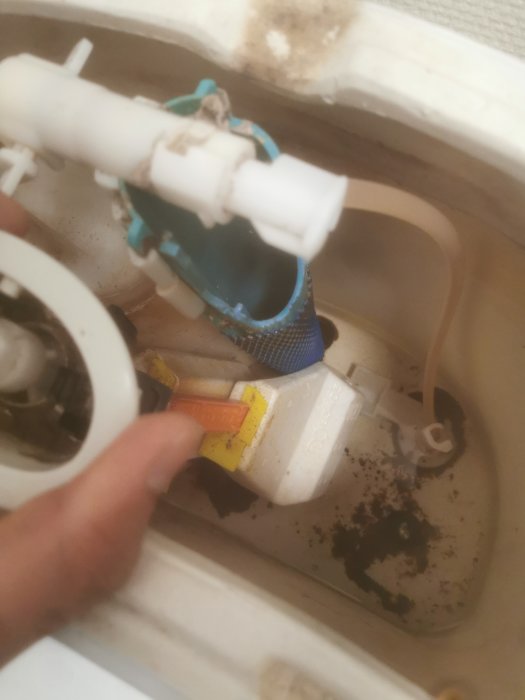 En söndrig platsventil i en toalettcistern med synlig skada, omgiven av vattenledningar och korrosion.