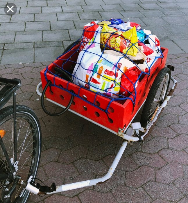 Ombyggd cykelvagn med röd plywood och limträsidor lastad med matkassar säkrade med ett blått nät.