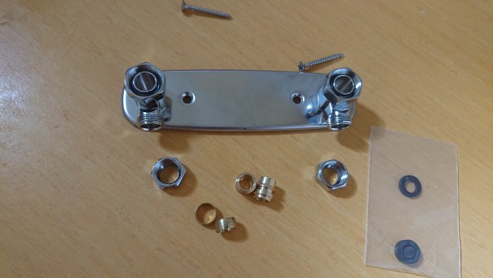 Delar till badkarsblandare på träbord inklusive blandarfäste, klämringar och packningar.