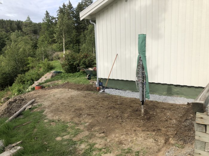 Nyligen avslutad dränering med grus och isolering längs en husgrund på en terrasserad gräsmatta.