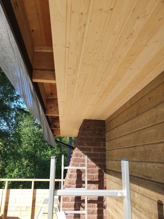 Nybyggd takfot med utomhushögtalare och träpanel vid källaringång med synlig tegelvägg.