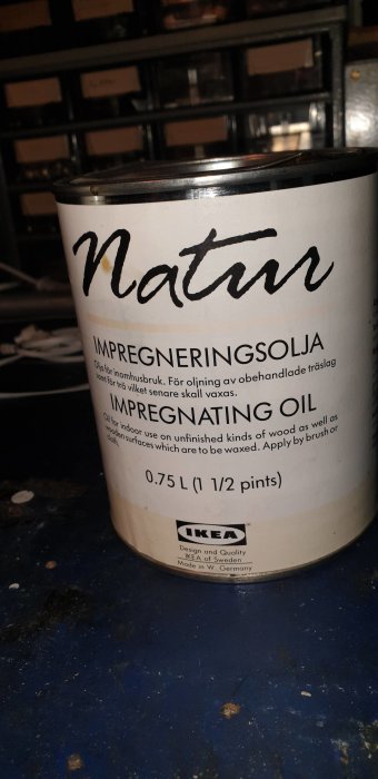 Burk med texten "Natur IMPREGNERINGSOLJA" för träoljning före vaxning, med IKEA-logotyp, på smutsigt blått underlag.