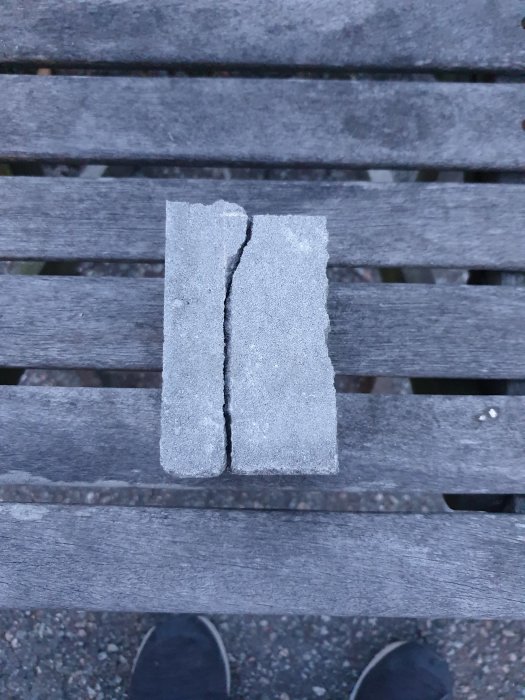 En ojämnt klippt betongsten delad i två delar placerad på en bänk, med synliga skor i förgrunden.