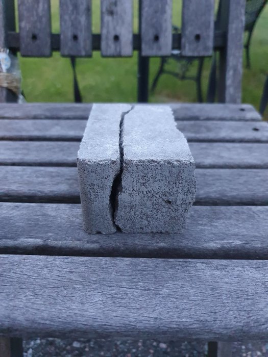 Betongsten som är ojämnt klippt i två delar med synlig spricka, placerad på ett träbord utomhus.