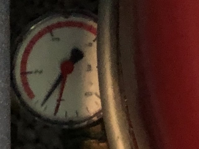 Närbild av en manometer med visare som indikerar lågt tryck, delvis skymd av suddig röd kant.