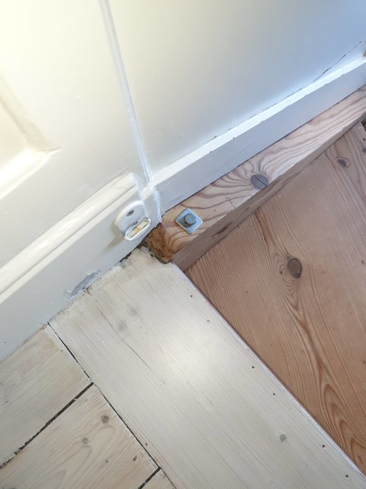 En skruv med en fyrkantig bricka på trägolv vid foten av en vitmålad U-trapp i ett äldre hus.