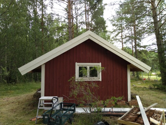 Rött trähus med nyinstallerade vitmålade vindskivor på takets gavel i skogsmiljö.